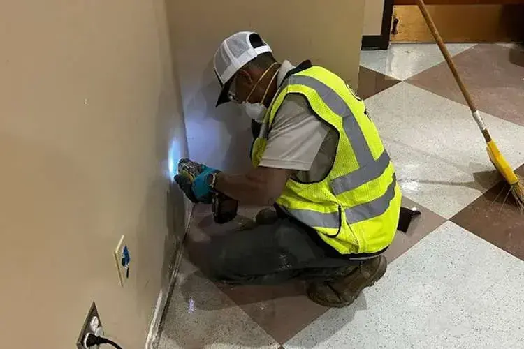 Technician in a safety vest checking a wet wall with a moisture meter in a Goose Creek home