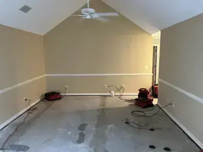 Empty room with a bare concrete floor and air movers running after the carpet came out in a Hanahan home