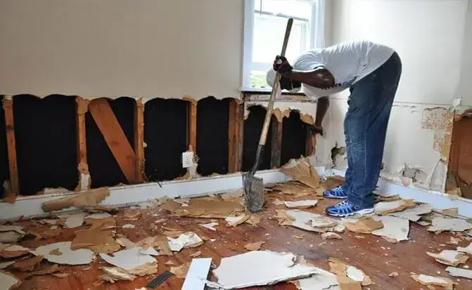 Man removing wet drywall from the lower walls of a room after flooding