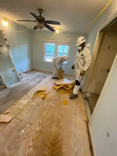 Workers in protective suits pulling up wet subflooring in an emptied room