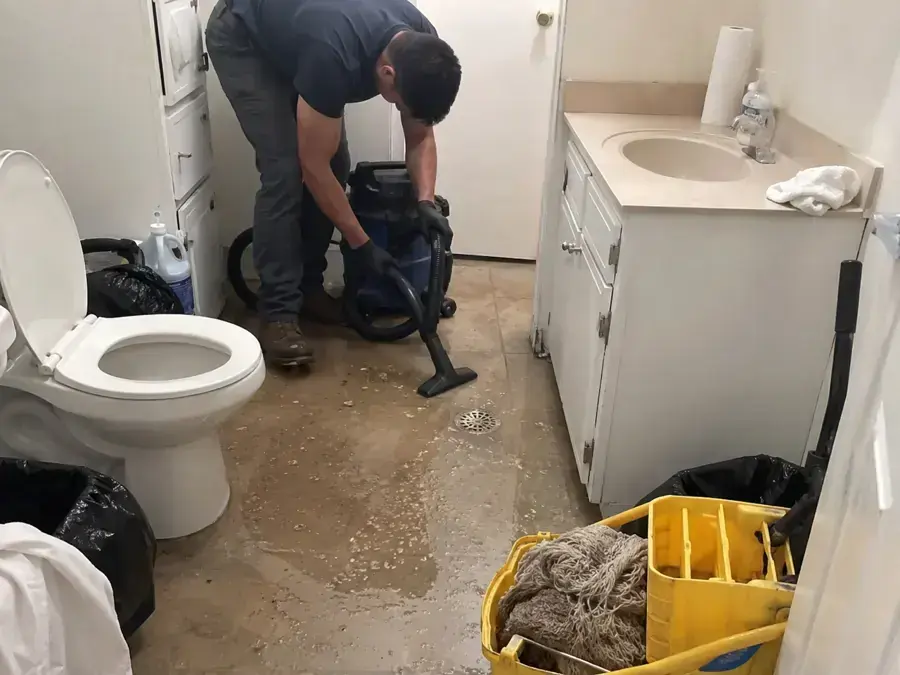 Technician vacuuming water off a bathroom floor beside the toilet and vanity, bathroom leak water damage in Goose Creek