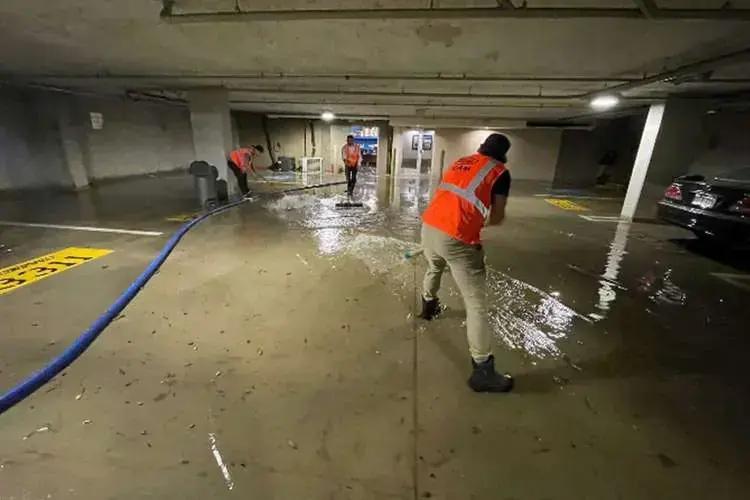 Worker pulling standing water across a flooded concrete floor with an extraction hose, water extraction in Goose Creek