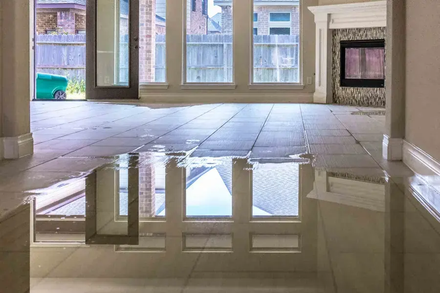 Floodwater standing across a tiled living room floor beside a fireplace after heavy rain, storm water damage in Goose Creek