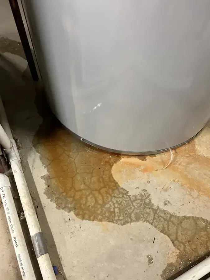 Rusty water spreading across a concrete floor from the base of a water heater, water heater leak in Goose Creek
